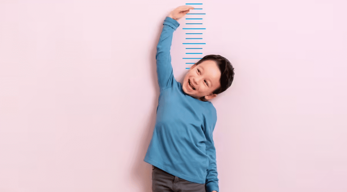 é trai mặc áo xanh đang đo chiều cao trên tường, thể hiện quá trình phát triển chiều cao khỏe mạnh